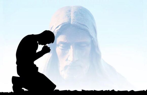 A silhouette of a person kneeling and praying in front of a large, semi-transparent image of Jesus Christ with a gentle expression.