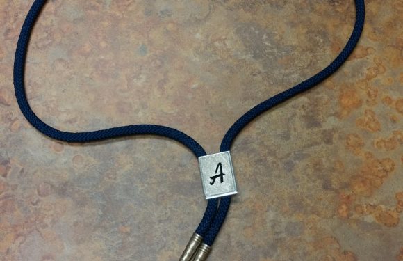 A navy blue lanyard with a small rectangular metal clip labeled "A" and three metal tips, resting on a textured brown surface.