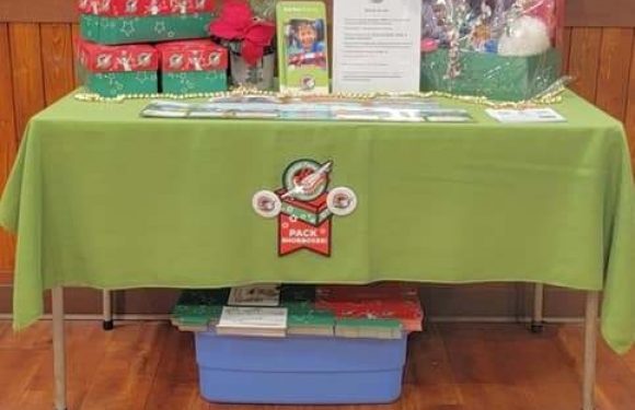 A table covered with a green tablecloth displays gift baskets, balloons, and various items in a restaurant setting. Behind, there's a wooden sign reading "PIZZA RANCH" and a metal star on a blue wall.