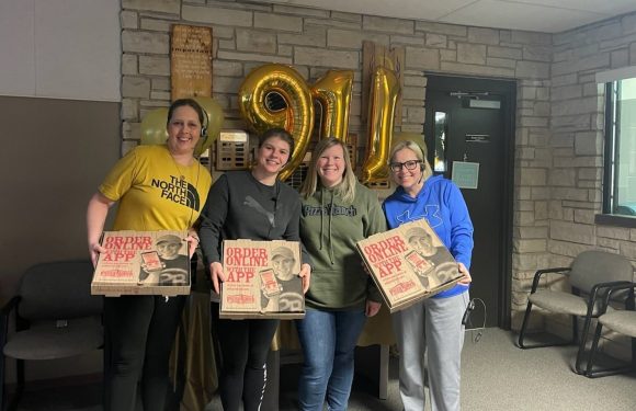Four women stand indoors holding Pizza Ranch pizza boxes, smiling in front of large gold balloons forming the number "2021" against a brick wall.