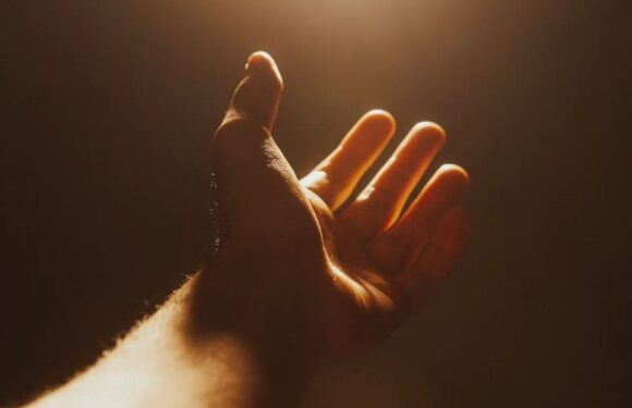 A hand reaching towards a warm, glowing light source, cast in soft shadows with a dark background and a small logo of Pizza Ranch at the bottom.