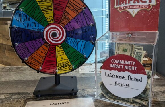 A colorful spinning wheel with sections labeled by various prizes, a donation jar labeled "Community Impact Night" with cash, and a sign requesting $2 donations for a cause.