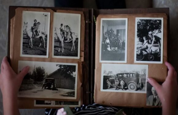 Black and white photos in a vintage photo album, including children playing on a horse, a group indoors with a Christmas tree, and an old car parked outside.