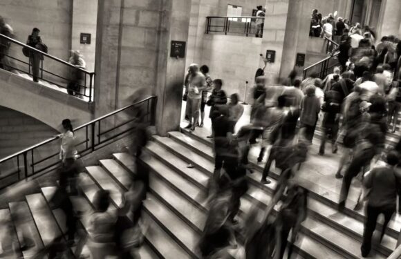 Crowded staircase and escalators in a busy indoor public space with many people walking and standing around.