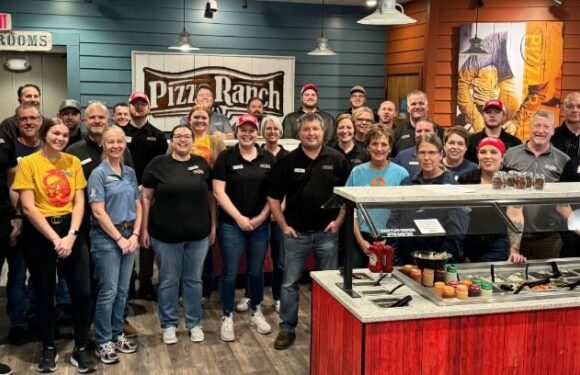 Group of employees standing inside a Pizza Ranch restaurant with colorful walls, signage, and a buffet counter in front.