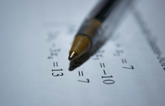 Close-up of a yellow-tipped pen marking an answer on a math worksheet with equations. The worksheet features simple algebra problems.