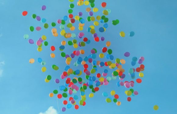 Colorful balloons floating against a bright blue sky with a few clouds.