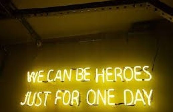 A neon sign in yellow reads "WE CAN BE HEROES JUST FOR ONE DAY" against a dark background.