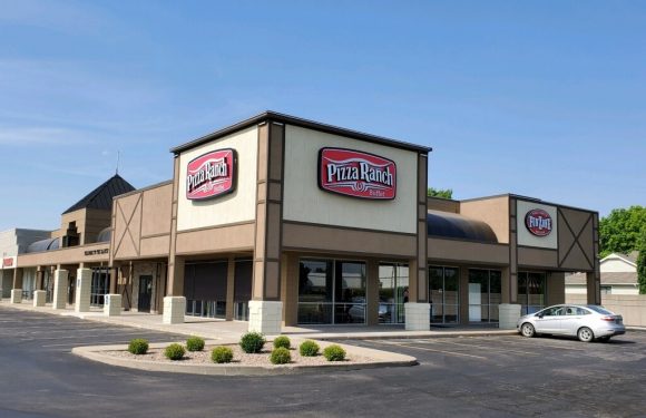 A single-story commercial building housing a Pizza Ranch buffet, with multiple signs displaying the logo, a parking lot, and a silver car parked outside.