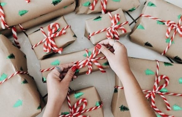 Hands wrapping Christmas presents in brown paper with green trees and red-and-white striped ribbon.