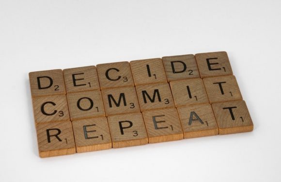 Scrabble tiles spell out "DECIDE COMMIT REPEAT" on a white background, with some tiles showing point values.