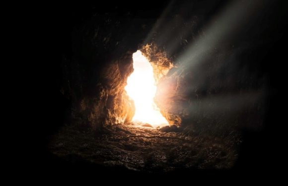 Bright sunlight shining through the entrance of a dark cave, creating rays of light and illuminating the rocky interior.
