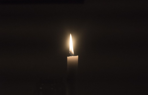 A lit white candle with a gentle glow against a dark background.