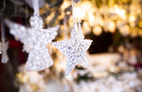 Shiny snowflake and star-shaped ornaments hanging on a display with blurred warm lights in the background.