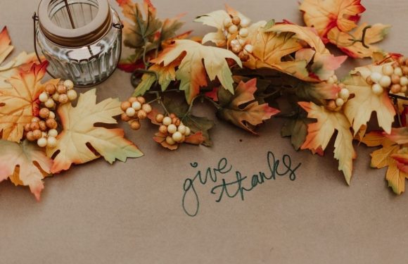Autumn leaves, berries, a candle, and a handwritten "give thanks" message on kraft paper.