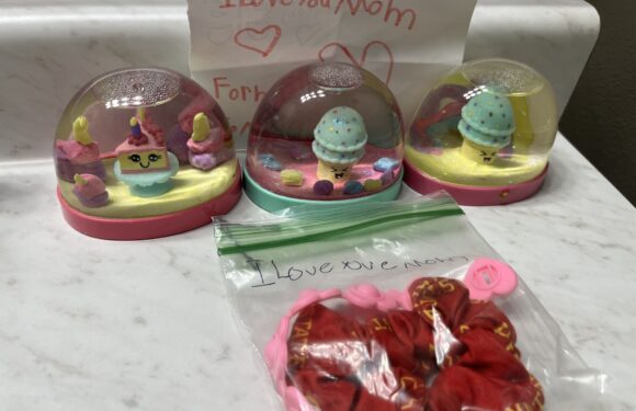 Three small dome-shaped toys with pastel colors and cute faces, a handwritten note saying "I love you Mom," and a red scrunchie in a plastic bag are displayed on a white surface.
