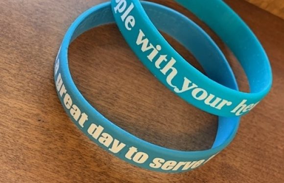 Two blue silicone wristbands with white text, placed on a wooden surface with a wooden edge in the background.
