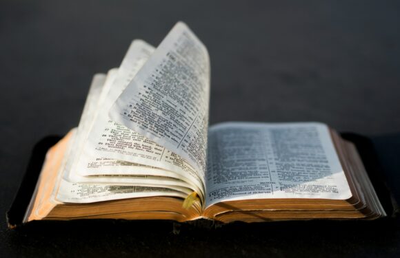 An open Bible with a black background, pages slightly lifted in the middle, showing text in a two-column format.