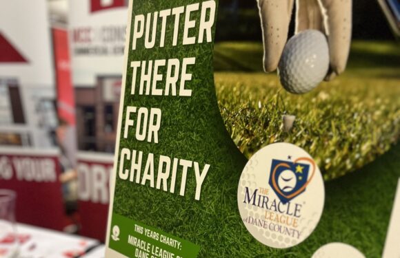 A golfer's hand holding a golf ball near a tee on a grassy course, with a charity flyer promoting a charity event for the Miracle League of Dane County, featuring a golf course background.