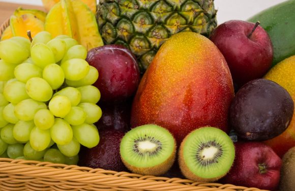 A basket of assorted fresh fruits including green grapes, pineapples, kiwis, apples, mangoes, and a pear.