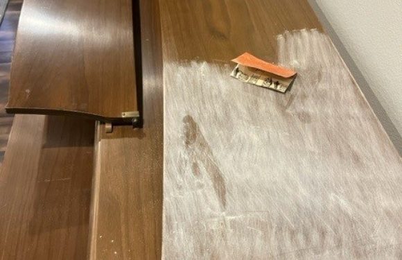 A wooden counter with a dusting of white powder on one side, a small orange tag, and a metal screw protruding from the surface.
