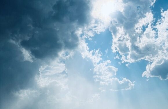 A partly cloudy sky with rays of sunlight breaking through clouds over an empty, freshly paved road stretching into the distance.