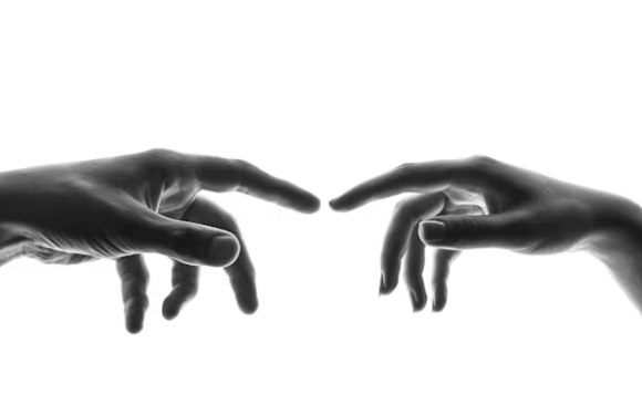 Two hands reaching towards each other with fingers almost touching, set against a plain white background.