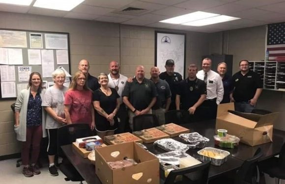 Group of people, including staff in black uniforms with Pizza Ranch logos, standing behind a table with pizza boxes and food trays in a meeting room.