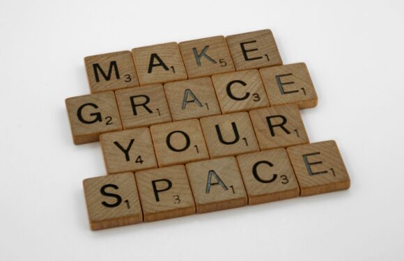 Wooden tiles spell out "MAKE GRACE YOUR SPACE" on a white background. Some tiles have letter values similar to Scrabble.