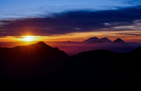 A vibrant sunrise over mountains with colorful sky hues, casting a warm glow on the silhouetted peaks and valleys.