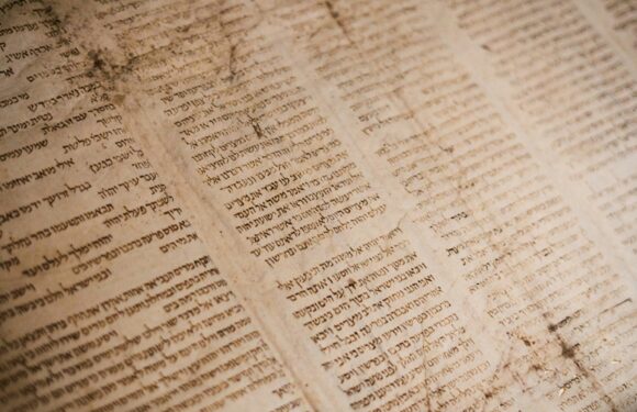 Ancient parchment with handwritten text in Hebrew, aged and stained, laid out flat on a surface.
