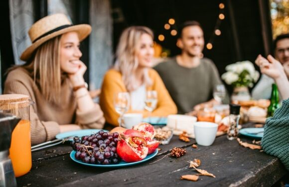 A group of people gathered at an outdoor table, enjoying food and drinks, with one person wearing a straw hat and casual clothing.