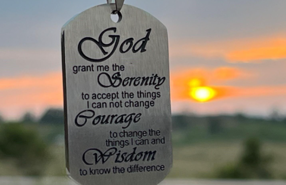 A metal tag hanging with an inspirational prayer: "God grant me the serenity to accept the things I cannot change, courage to change the things I can, and wisdom to know the difference," with a sunset in the background.