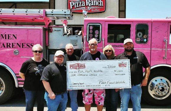 Group of six people standing in front of a pink Pizza Ranch fire truck, holding a large check for $1,000 made out to Park Hills Wichita.