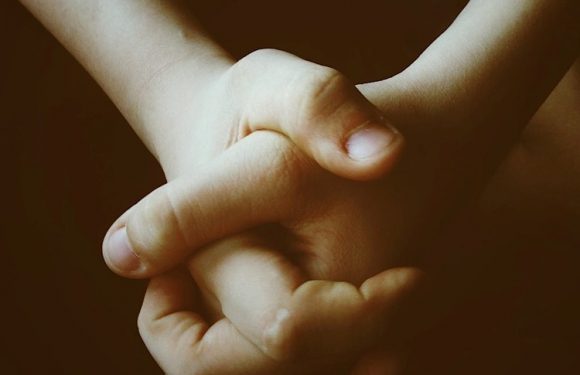 Two children’s hands are clasped together in a warm handshake, with a dark background. The children are wearing short-sleeved uniforms with the Pizza Ranch logo.