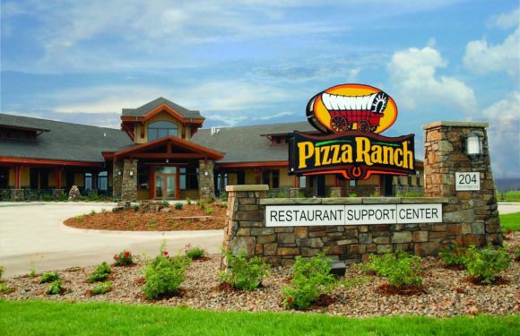 A large stone sign with a colorful pizza wagon logo reads "Pizza Ranch" and "Restaurant Support Center" in front of a modern, ranch-style building on a sunny day.