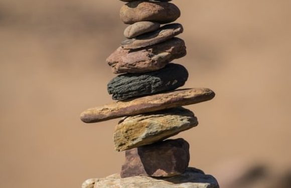 A tall stack of variously colored and textured stones balanced on top of each other outdoors against a blurred background.