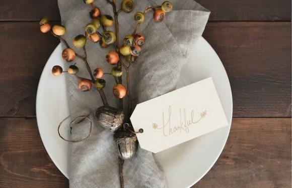 A napkin with branches of berries and a "thankful" tag, arranged on a white plate over a dark wooden table.