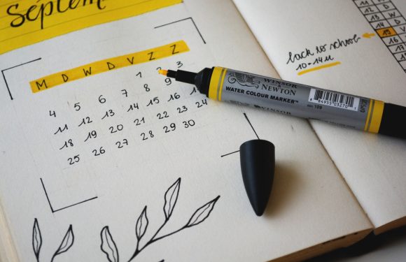 A handwritten calendar page for September, with a yellow highlighter marking the days of the week, and a black marker pen resting on an open planner with notes.
