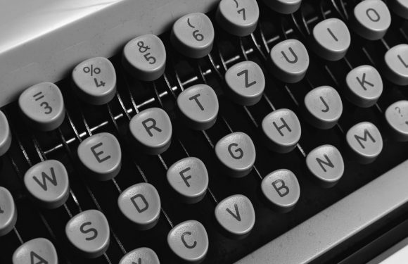 Close-up of a vintage typewriter keyboard in black and white, showing keys with letters, numbers, and symbols.