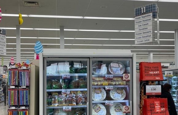 Shelf with frozen pizzas inside a store, with red donation bags nearby and a sign overhead about giving back to local schools.