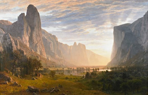 A scenic landscape featuring towering mountains, a river flowing through the valley, and a partly cloudy sky with warm sunlight illuminating the scene.