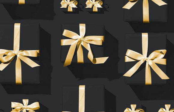 Several black gift boxes with shiny gold ribbons and bows are arranged on a dark surface, creating a festive and elegant display.