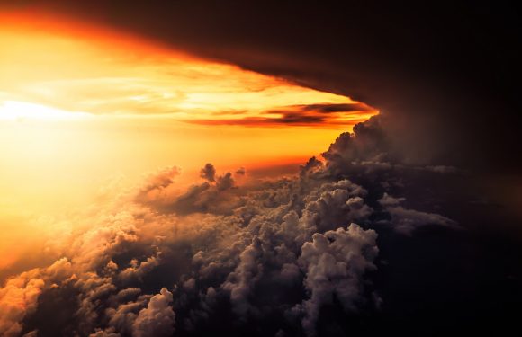 A dramatic sunset with bright orange and yellow hues illuminating clouds below, with dark storm clouds on the right side and a glowing horizon.