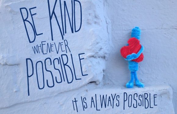 A white wall features a quote: "Be kind whenever possible, it is always possible" by Dala Lama, with a plush stuffed heart character holding its own heart nearby.