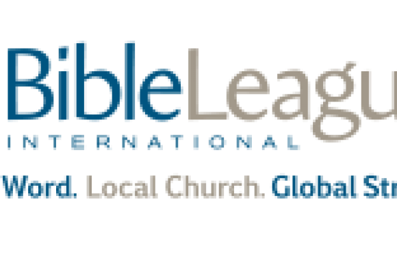 A group of people in blue and black uniforms standing outdoors on a concrete surface with trees in the background.