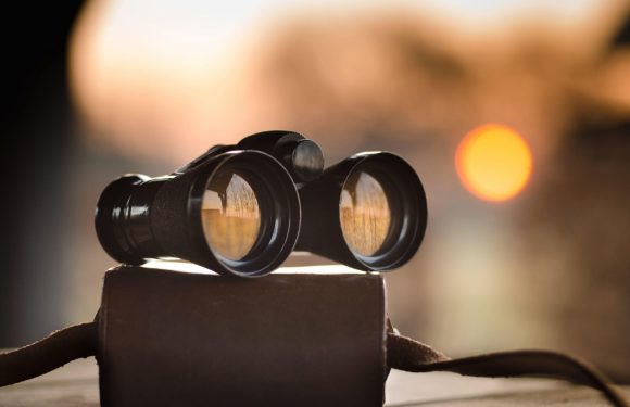 A pair of binoculars rests on a surface outside at sunset, with a blurred orange sun in the background.