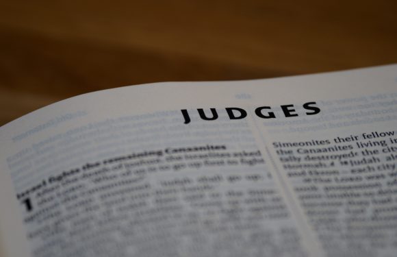 Close-up of a page titled "JUDGES" with blurred text on either side, likely from a religious or scriptural book, on white paper with slight curvature.