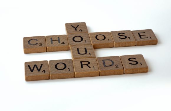 Wooden Scrabble tiles spelling out "CHOOSE," "WORDS," and "Y" on a white background.