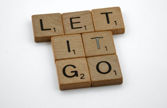 Scrabble tiles spelling out "LET IT GO" on a white surface.